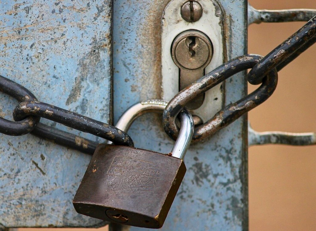 A weathered padlock and rusty chain secure a latch on a worn, light blue metal gate.