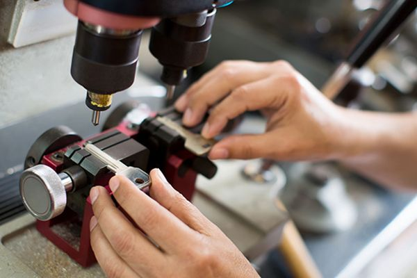 A Technician operates a drill on a machine in a key duplication service workshop.