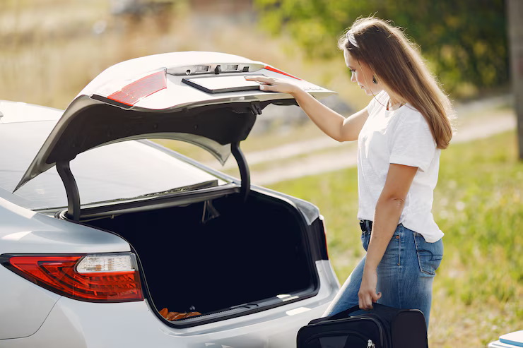 A woman stands beside her open car trunk, ready to load her luggage for a trip.