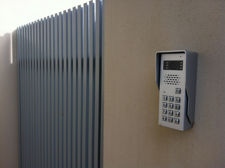 Intercom system installation featuring a telephone mounted on a wall beside a metal fence.