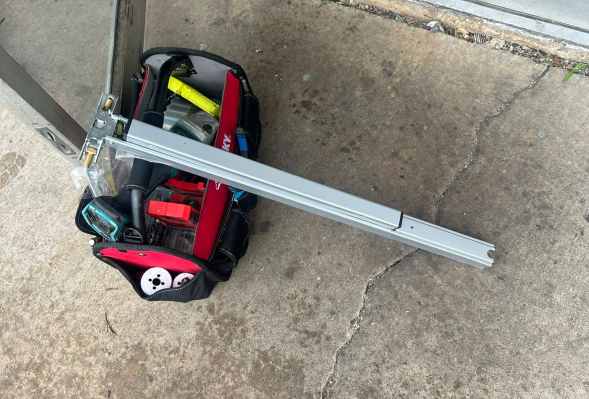 A person stands on concrete, next to a bag of tools marked All in 1 Locksmith Tools, ready for locksmith tasks.