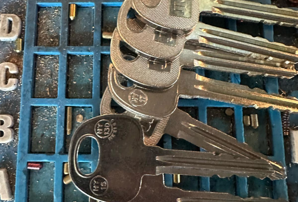 All in 1 Locksmith set of five stacked metallic keys on a blue tray with numbered grid sections and scattered small metal pins.